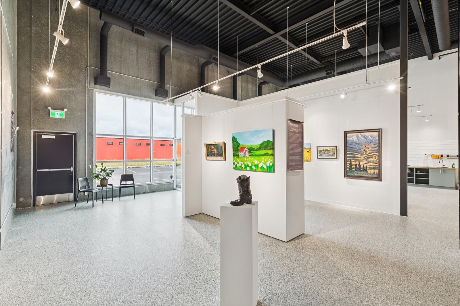 The Fig's community gallery: white walls of paintings under track lighting, a sculpture on a plinth and floor-to-ceiling storefront glass