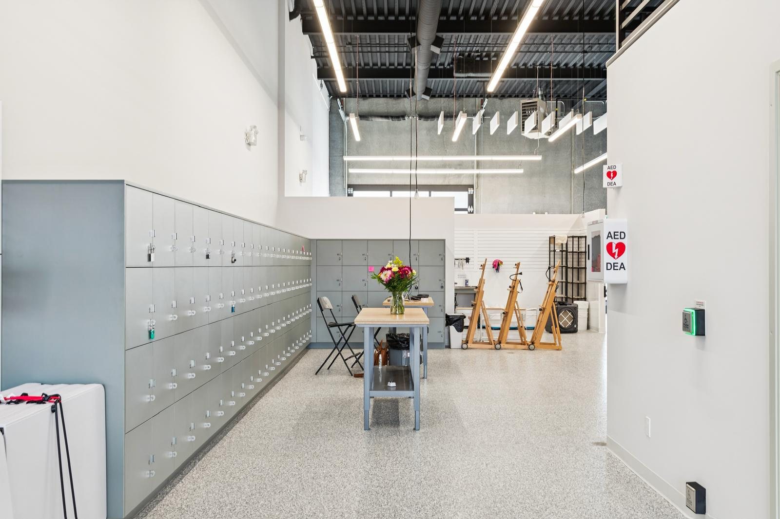 A wall of grey member lockers beside a work table with flowers and a row of easels