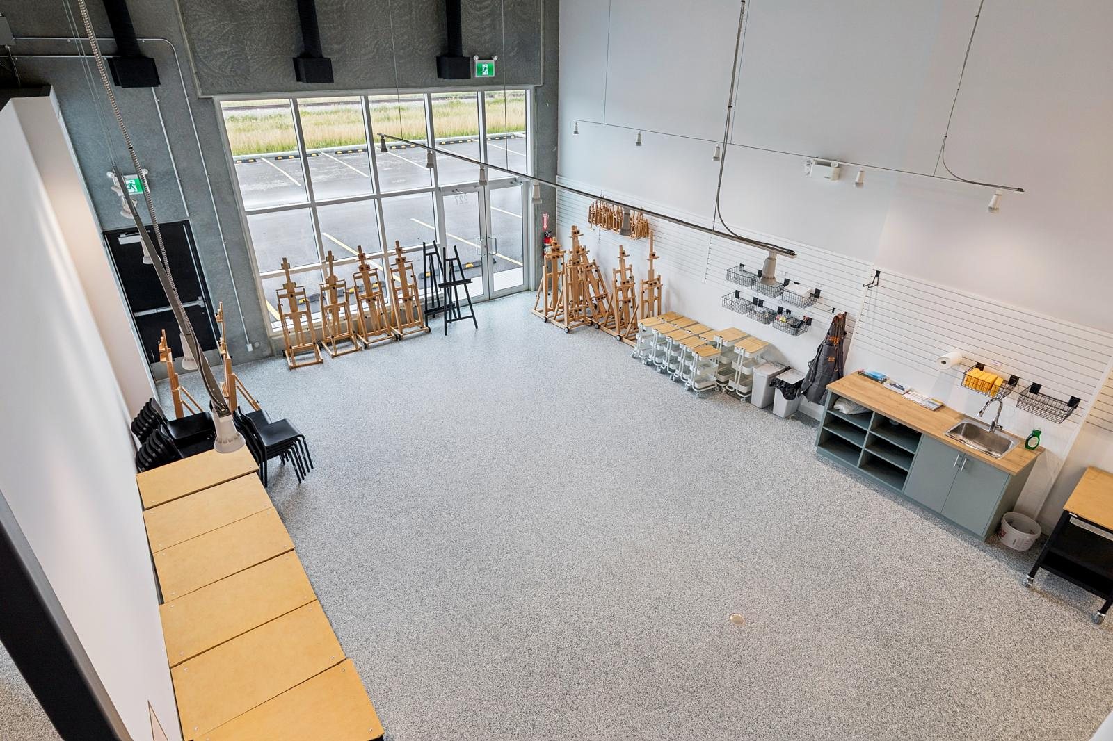 The studio floor seen from the mezzanine: rows of wooden easels, a sink counter and a two-storey glass storefront